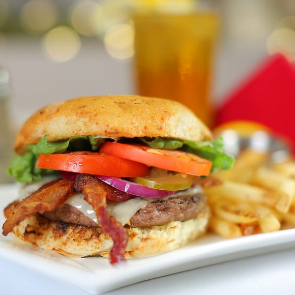 A bacon cheeseburger with lettuce, tomato, onion, and pickles, served with fries and a drink.
