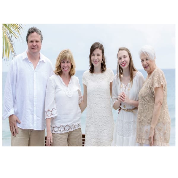 Five smiling people, three women and two men, posing outdoors with a body of water behind them.