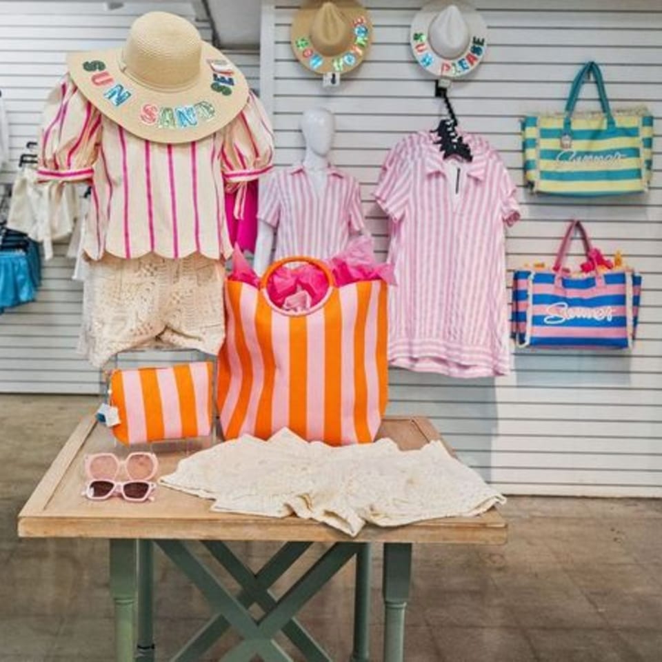 A display of summer clothing and accessories, including striped shirts, hats, and tote bags.