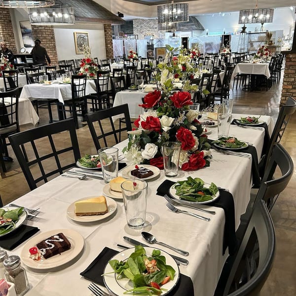 A dining room at The Potpourri House Restaurant set with white tablecloths, salads, desserts, and floral centerpieces.