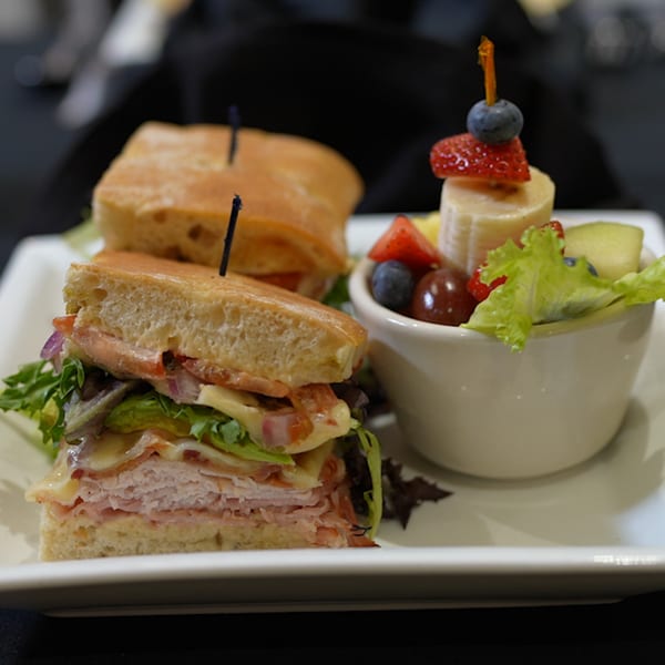A delicious American sandwich with a side of fresh fruit salad and greens on a white plate.